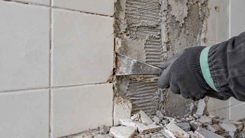 Špahtla odvaja pločicu od zida, vidi se češljasti sloj cementnog lepka